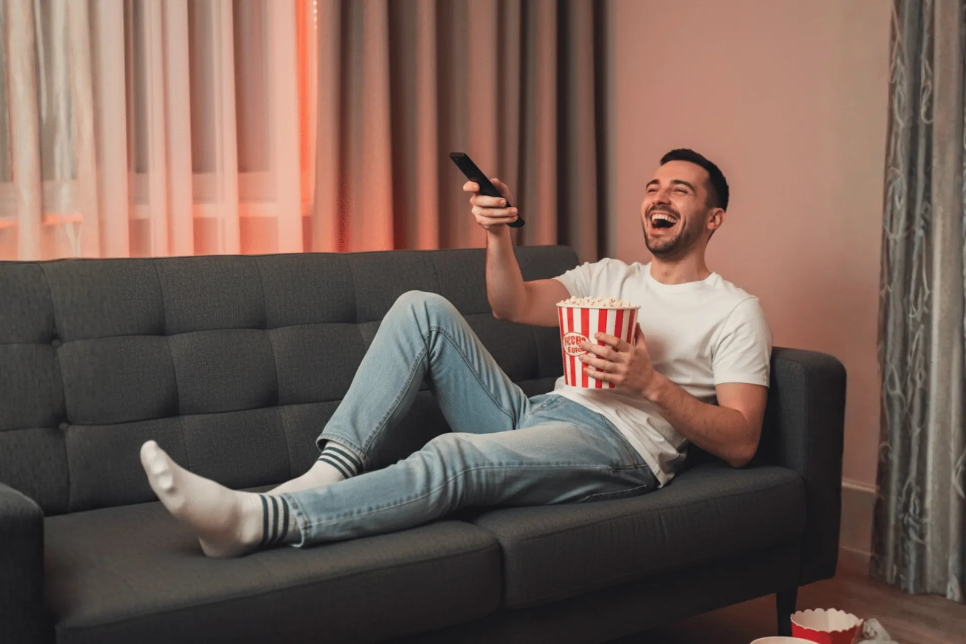 Homme profitant de l'expérience iptv vod à la maison, mangeant du pop-corn et regardant un film sur son canapé.